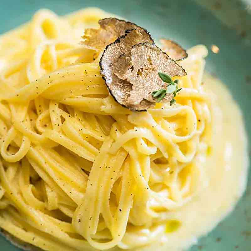 Pasta mit Trüffelcreme und Trüffelscheiben auf Teller.