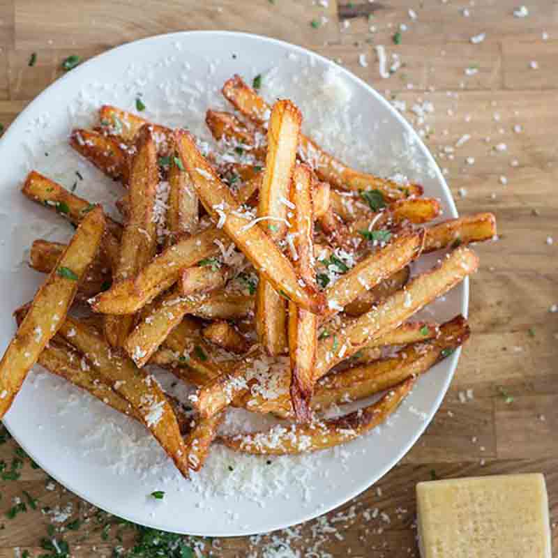 Pommes frites mit geriebenem Käse und Kräutern auf Teller.