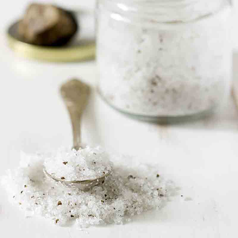 Trüffelsalz in Glas und Löffel auf weißem Hintergrund.