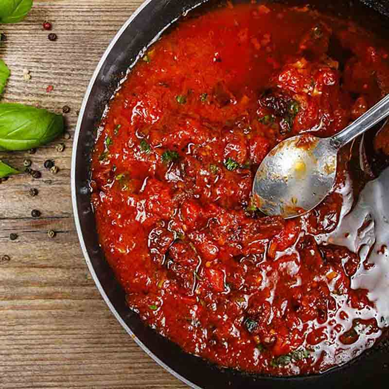 Tomatensugo in einem Topf. Daneben liegt ein Basilikum-Blatt.
