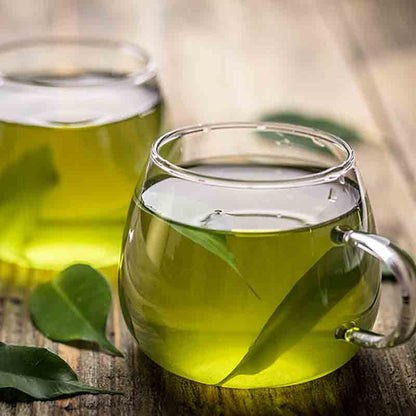 Zwei Gläser mit grünem Getränk und Blättern auf Tisch.