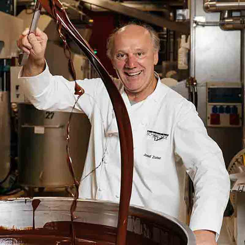 Josef Zotter taucht mit Schokoladenkelle in die gescholzene Schokolade