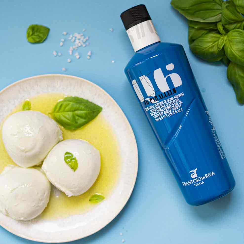 Olivenölflasche, Mozzarella, Basilikumblätter auf blauem Hintergrund.