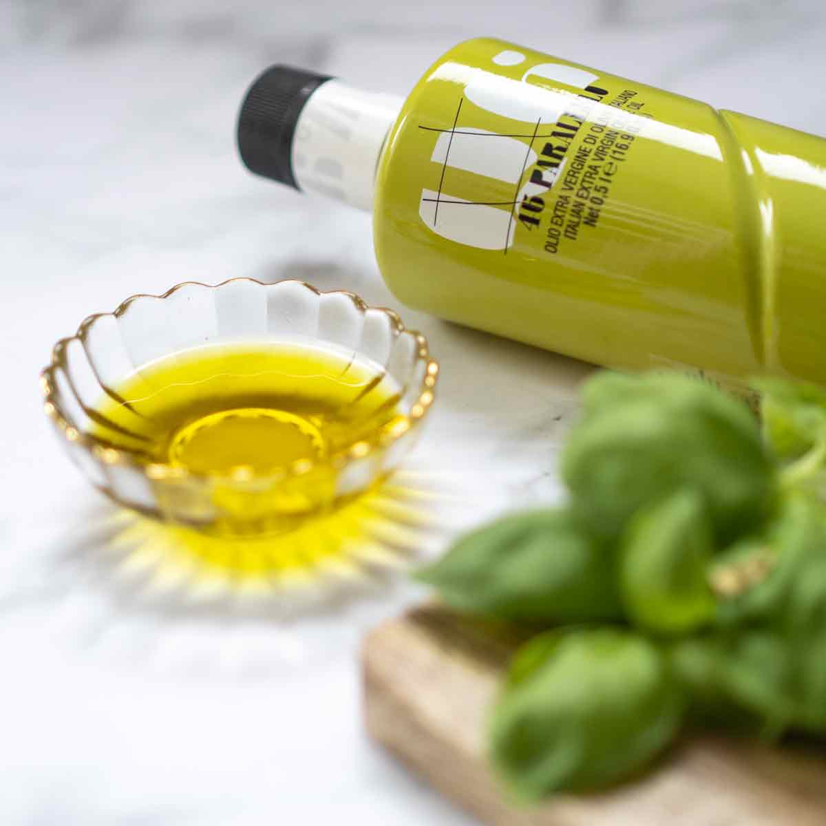 Olivenölflasche Agraria Riva Garda neben Schale und Basilikum.