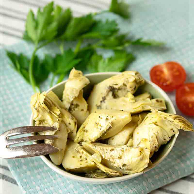 Artischockenherzen in Schale mit Kräutern und Tomaten.