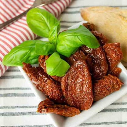 Getrocknete Tomaten mit Basilikum auf weißem Teller.
