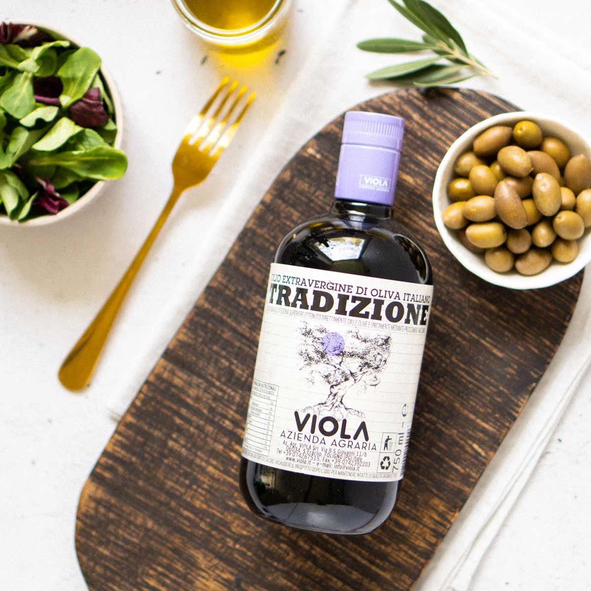 Olivenölflasche Viola, Oliven, Salat, Gabel auf Holzbrett.
