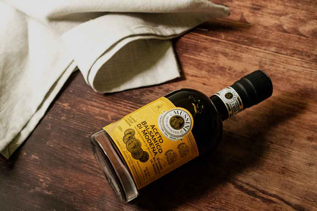 Aceto Balsamico Flasche auf Holztisch mit Tuch.