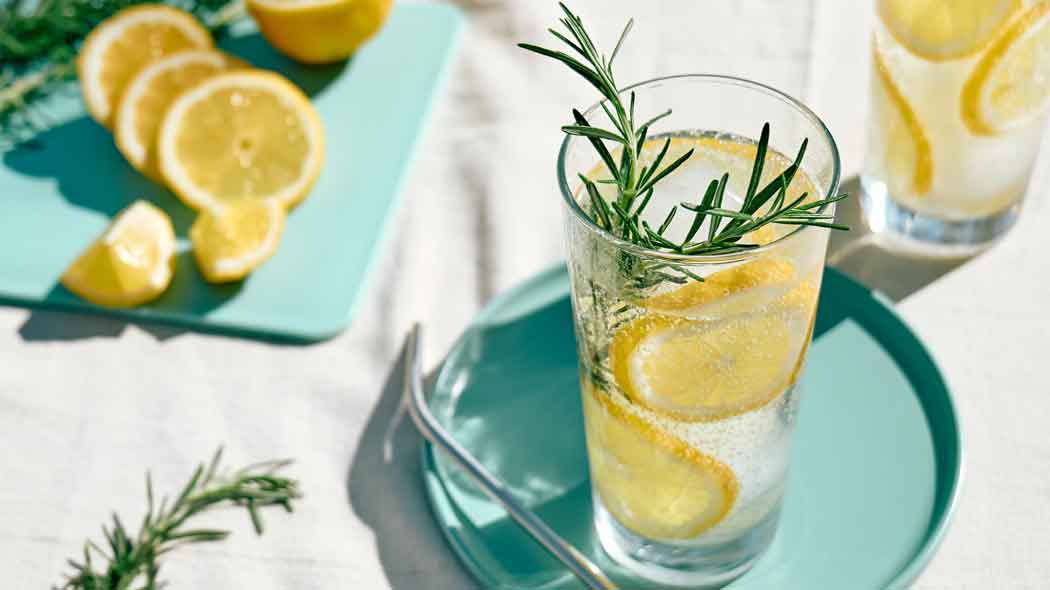 Zitronengetränk mit Rosmarin auf Tisch mit Zitronenscheiben.