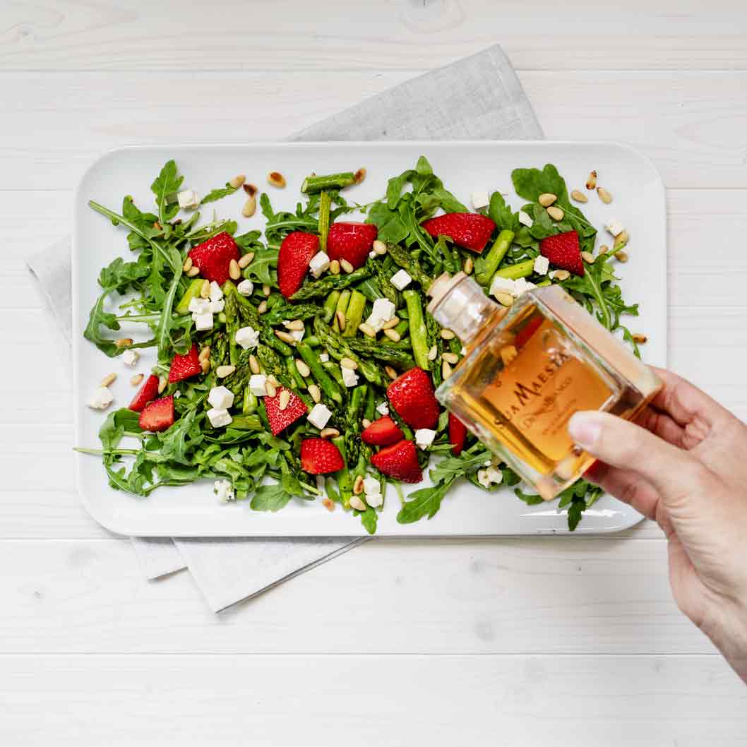 Hand hält Bellei Essig über Salat mit Erdbeeren.