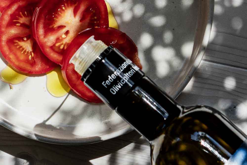 Olivenölflasche, Tomatenscheiben auf Teller, Schattenmuster sichtbar.