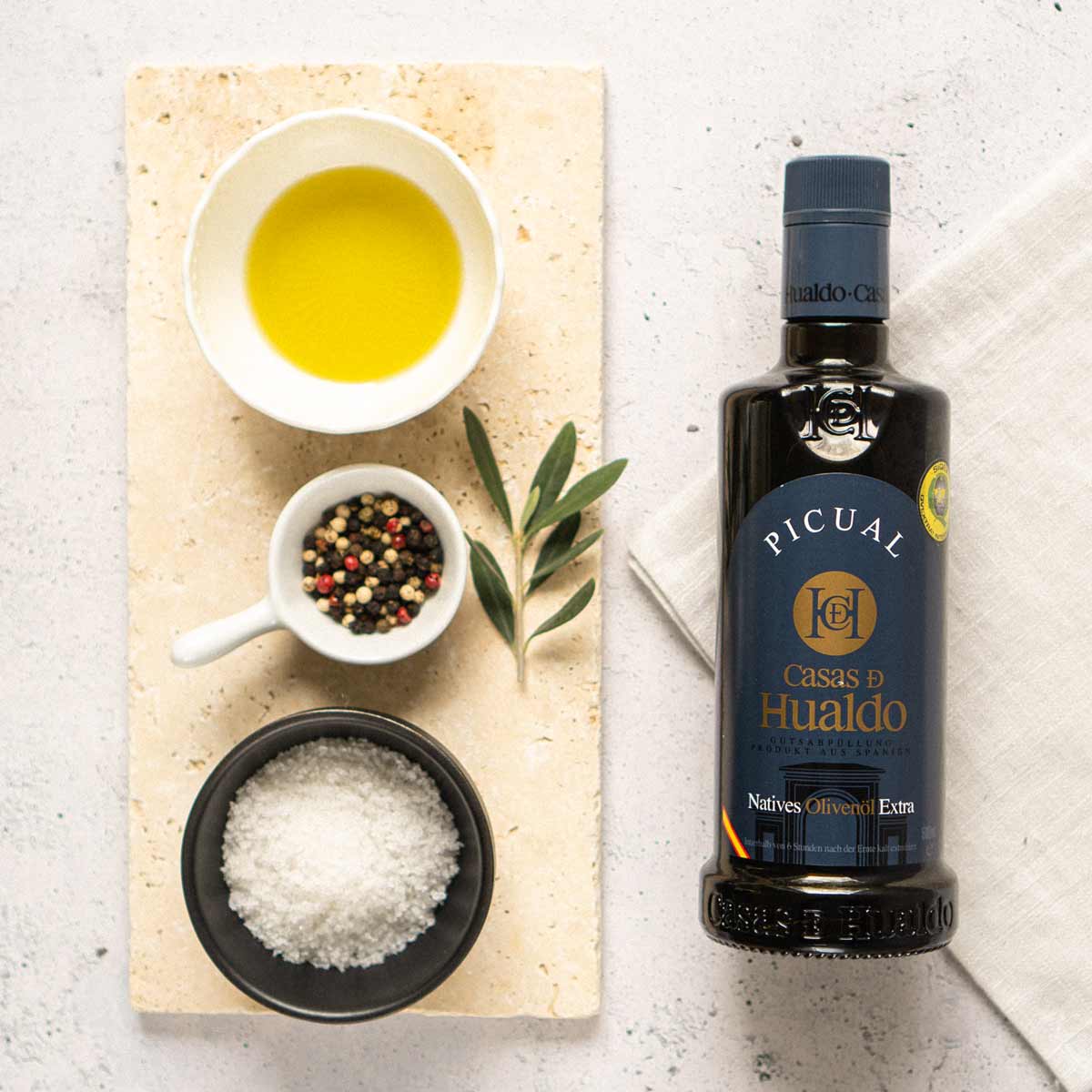 Casas de Hualdo Olivenöl mit Gewürzen und Olivenzweig.