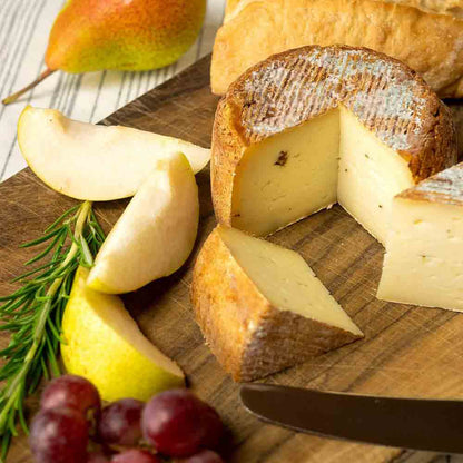 Käse mit Wacholderbeeren, Birne, Trauben, Rosmarin auf Holzbrett.