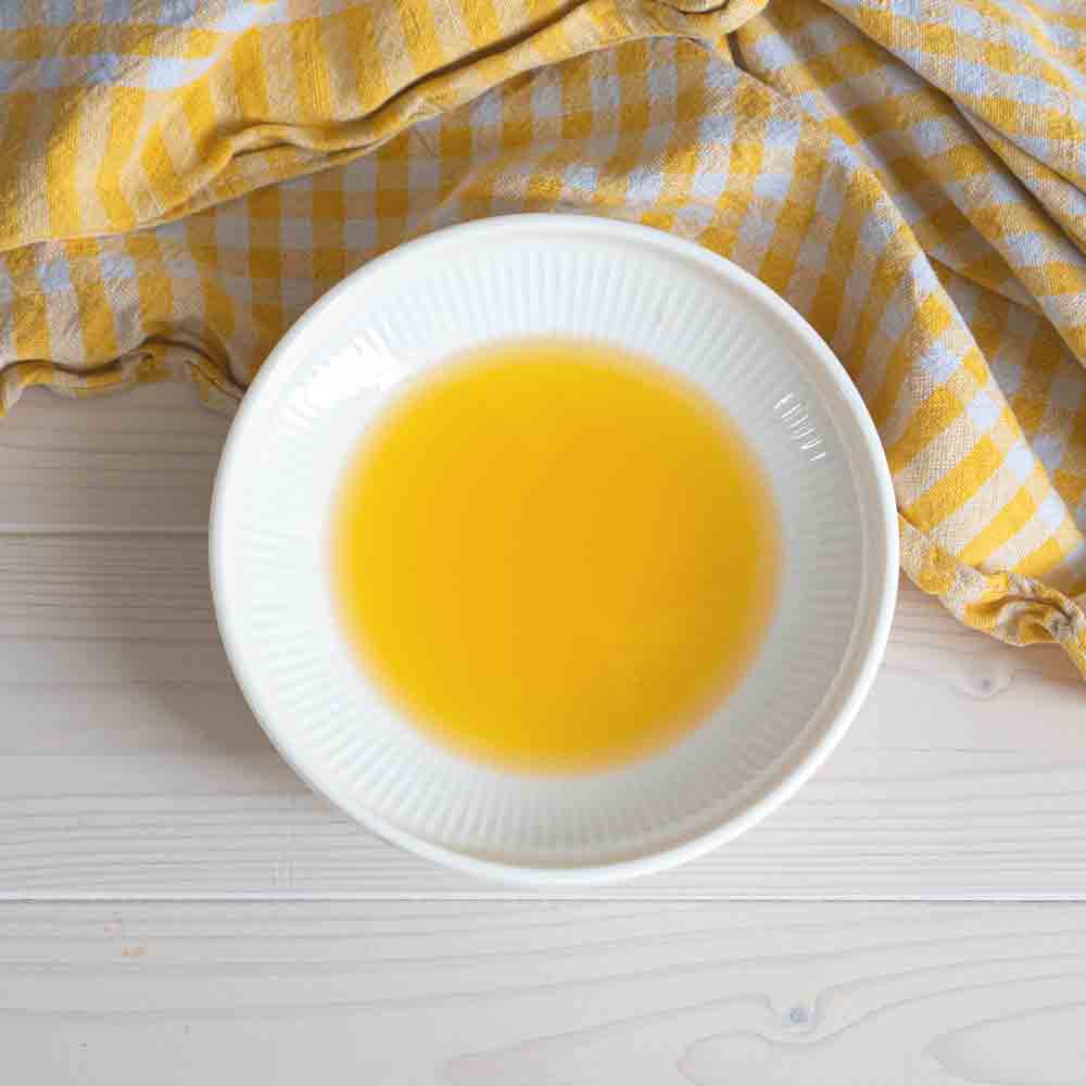 Schale mit gelbem Öl auf gestreiftem Tuch.