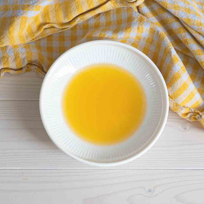 Schale mit gelbem Öl auf gestreiftem Tuch.