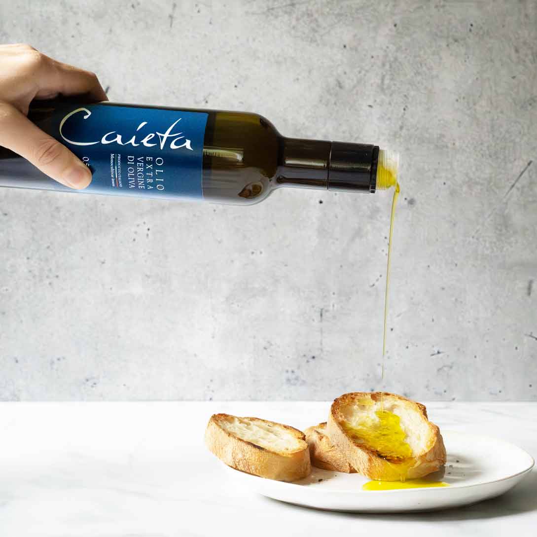 Olivenöl "Caieta" wird über Brot auf Teller gegossen.