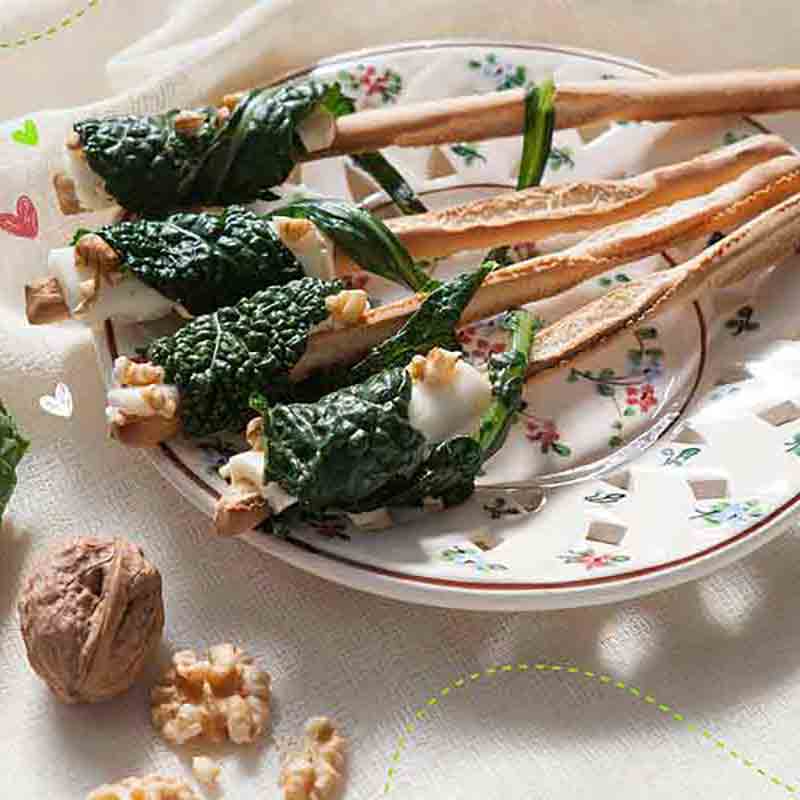 Grissini mit Käse, Walnüssen und grünem Blattgemüse auf Teller.