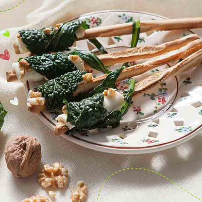 Grissini mit Käse, Walnüssen und grünem Blattgemüse auf Teller.