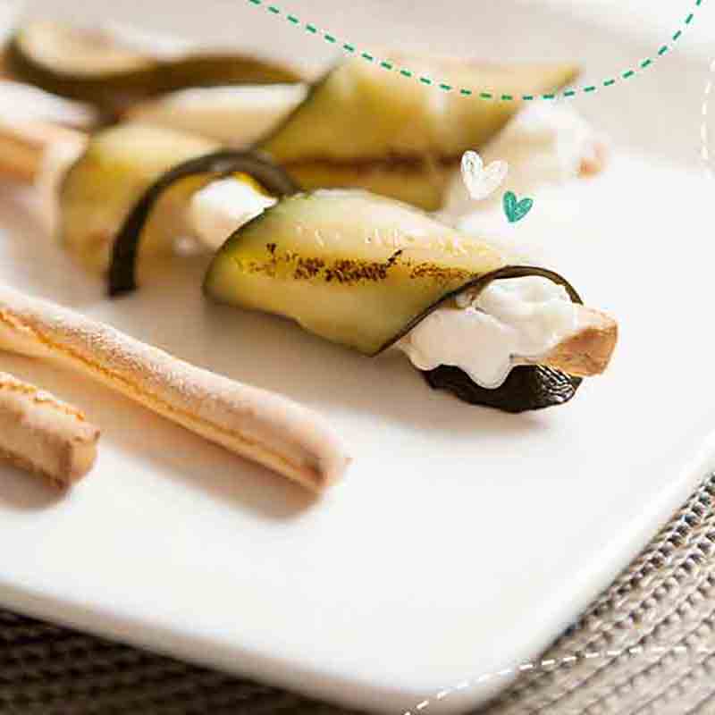Gefüllte Zucchiniröllchen mit Brotstangen auf weißem Teller.