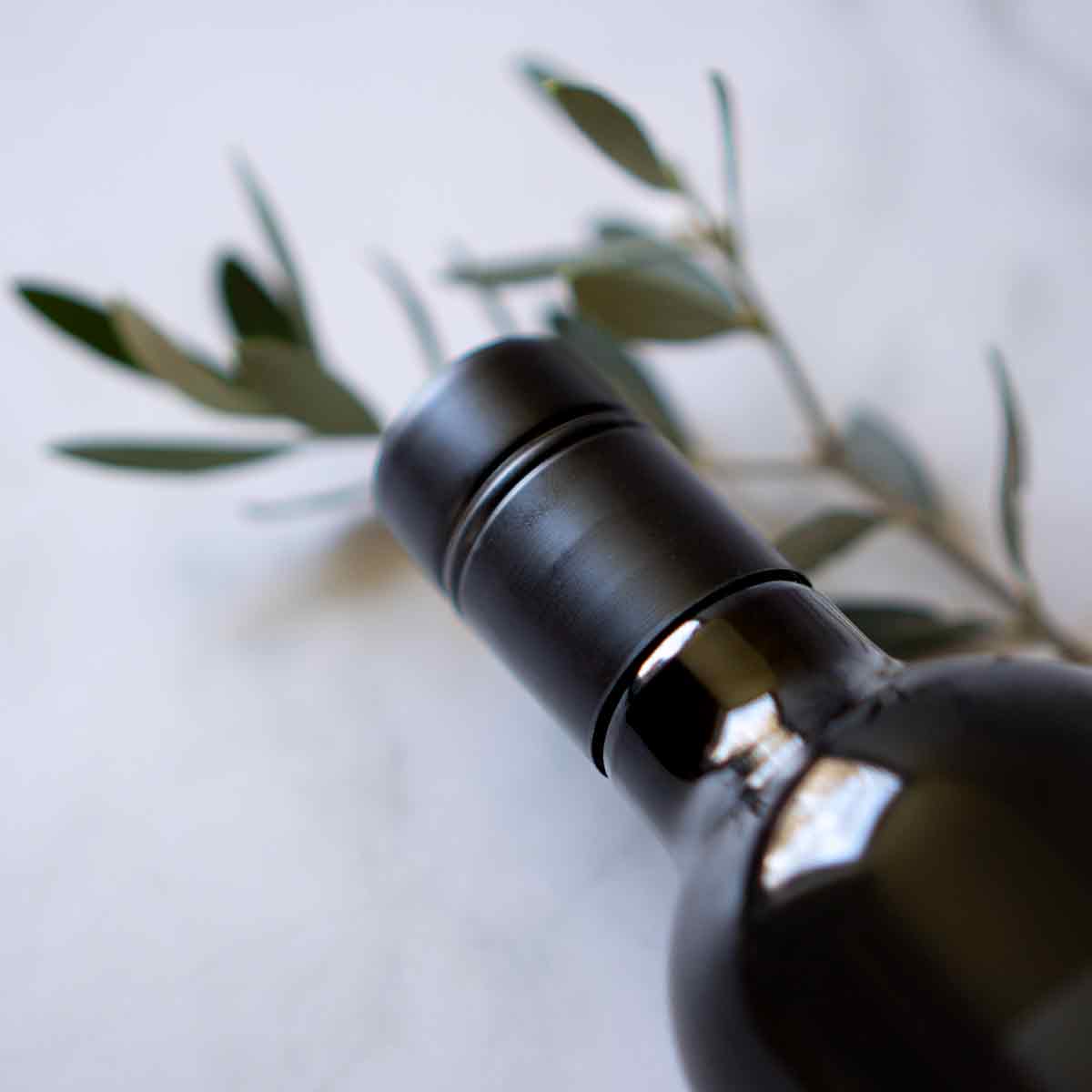 Olivenölflasche mit Olivenzweig auf hellem Hintergrund.