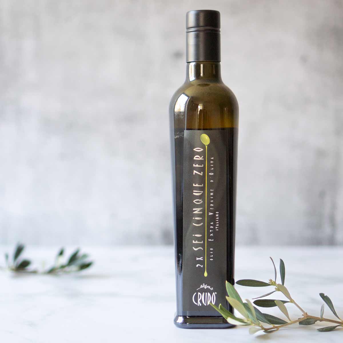 Olivenölflasche Crudo auf Marmor mit Olivenzweigen.
