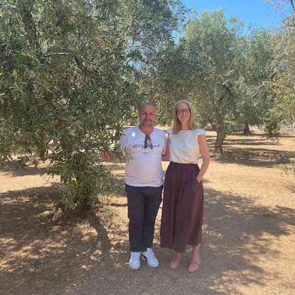 Andrea Jendral und ein Ölmüller stehen eng zusammen neben einem Olivenbaum im Olivenhain.