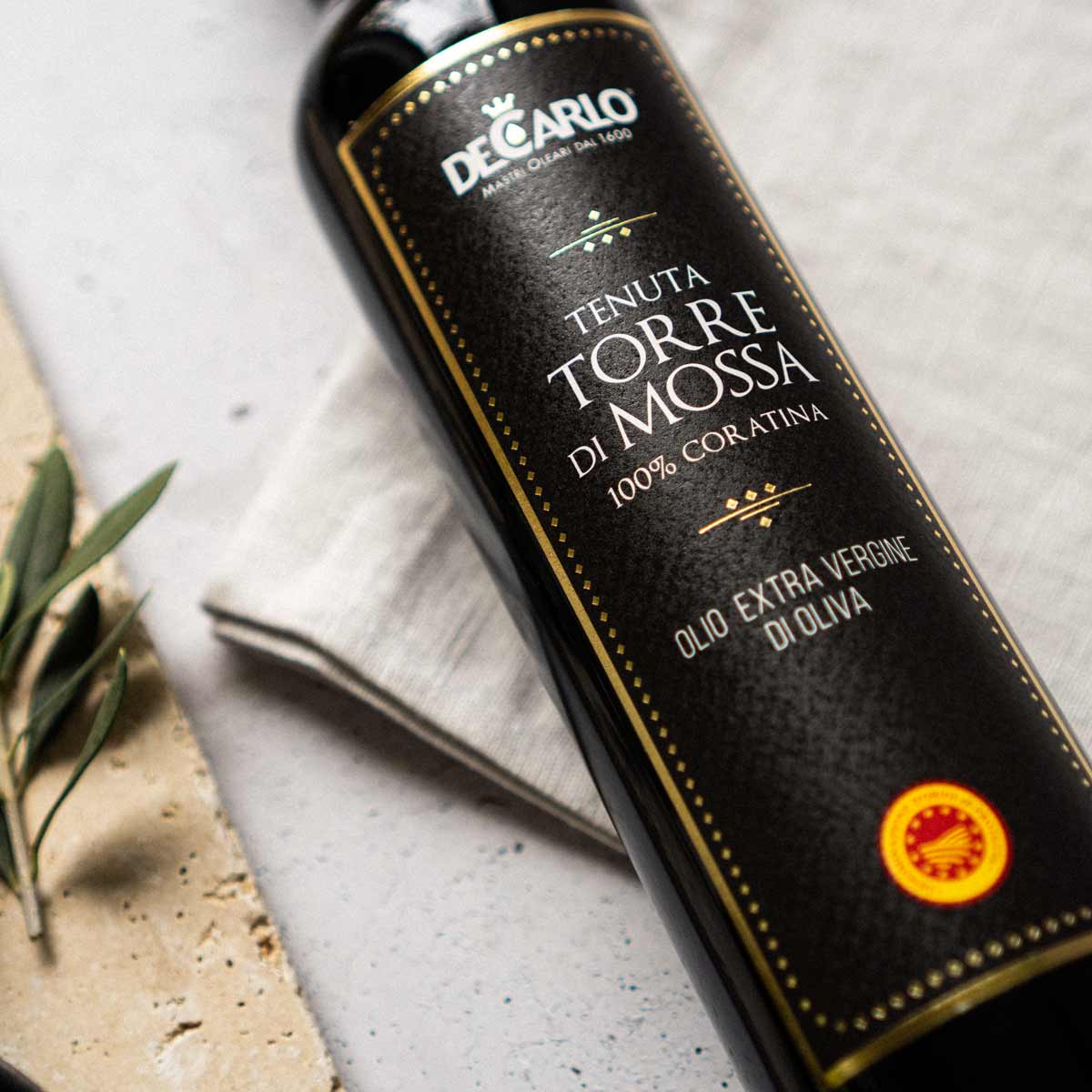 De Carlo Olivenölflasche mit Etikett auf hellem Hintergrund.