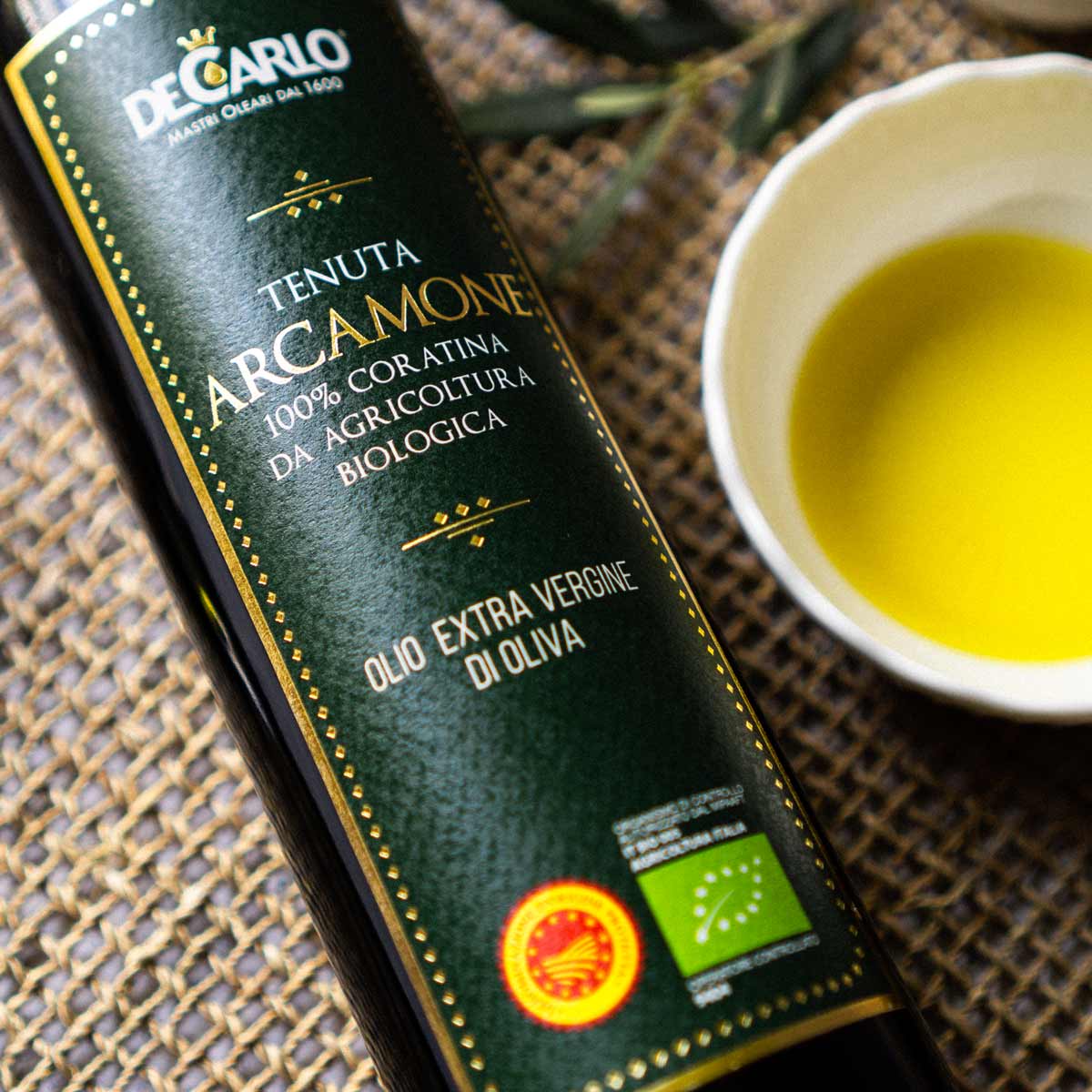 De Carlo Olivenölflasche neben Schale mit Olivenöl.