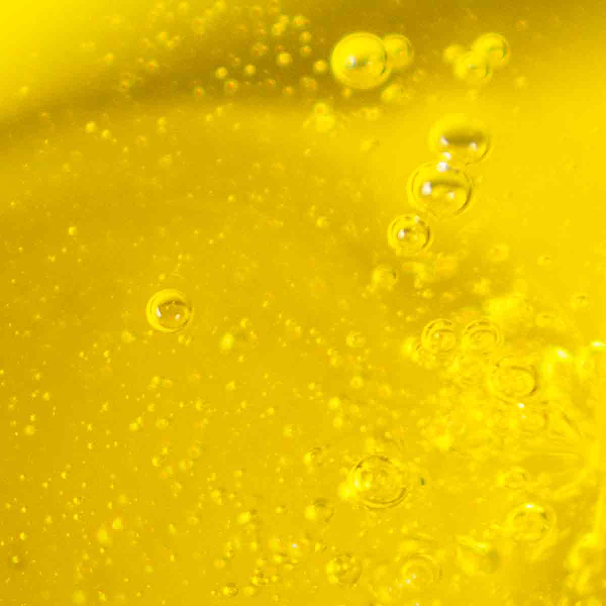 Nahaufnahme von dem goldgelben Olivenöl, dass durch das Eingießen kleine Bläschen mit Luft besitzt.