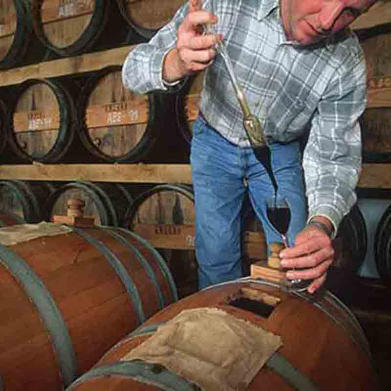 Mann prüft Essig in Weinkeller mit Holzfässern.