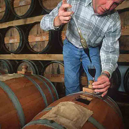 Mann prüft Essig in Weinkeller mit Holzfässern.