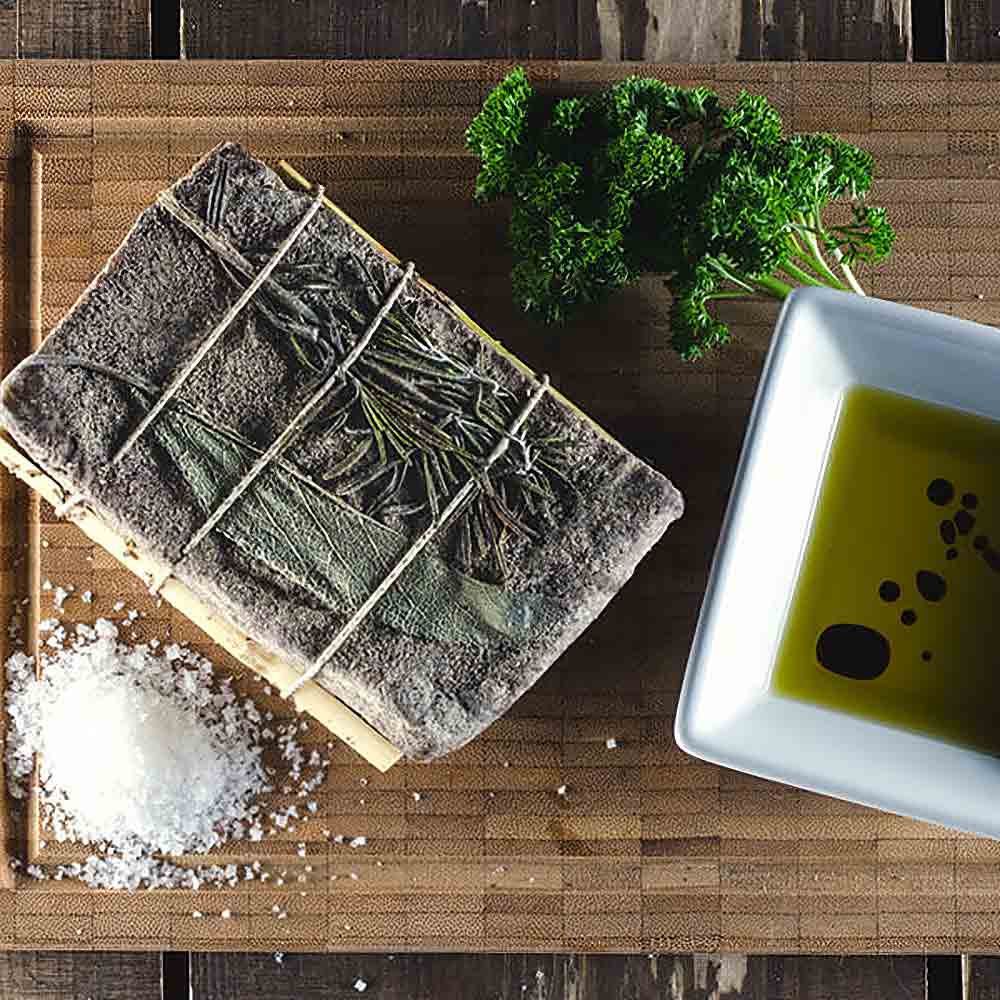 Pancetta, Olivenöl, Essig, Salz, Kräuter auf Holzbrett.