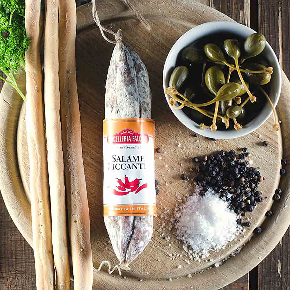 Salami, Grissini, Kapern, Salz, Pfeffer auf Holzbrett arrangiert.