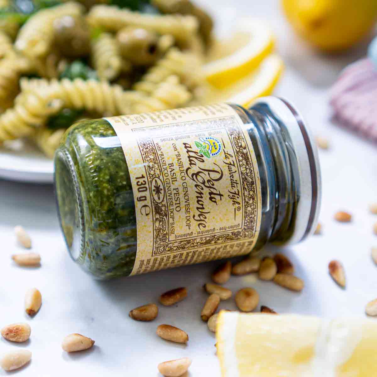 Favorita Pesto Genovese Glas neben Nudeln und Pinienkernen.