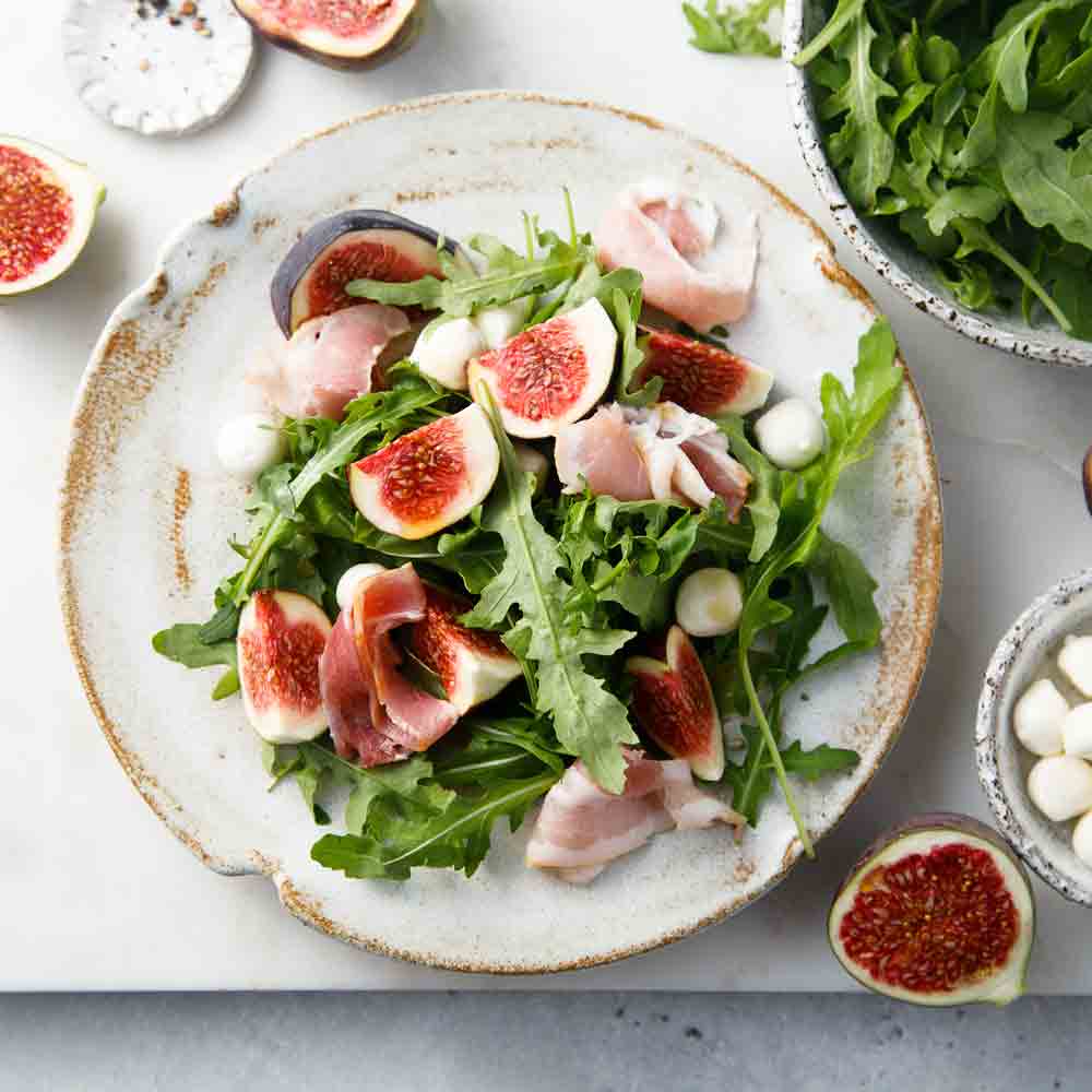 Rucola-Feigensalat mit Schinken und Mozzarella auf Teller.