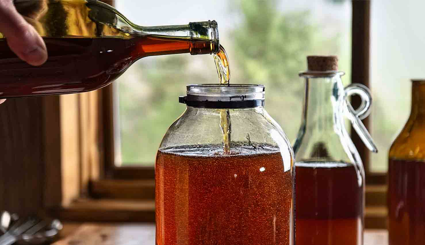 Essig wird in großes Glasgefäß gegossen, Holztisch.