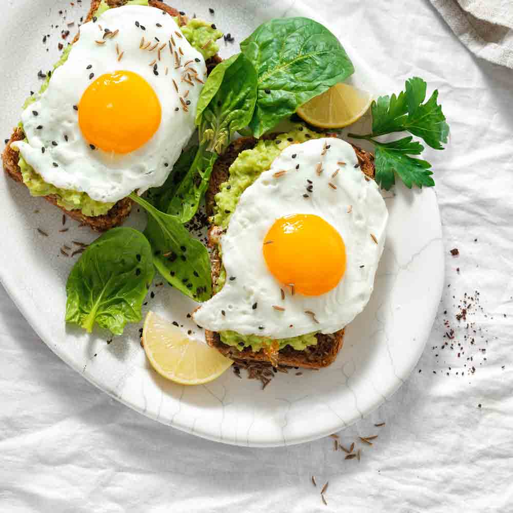 Zwei Spiegeleier auf Avocado-Toast mit Kräutern und Limette.