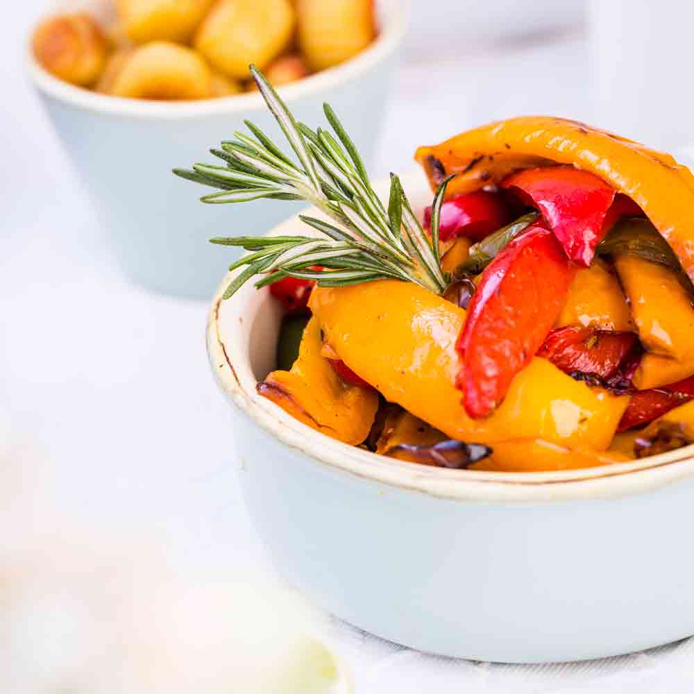 Gegrillte Paprika mit Rosmarin in weißer Schale serviert.