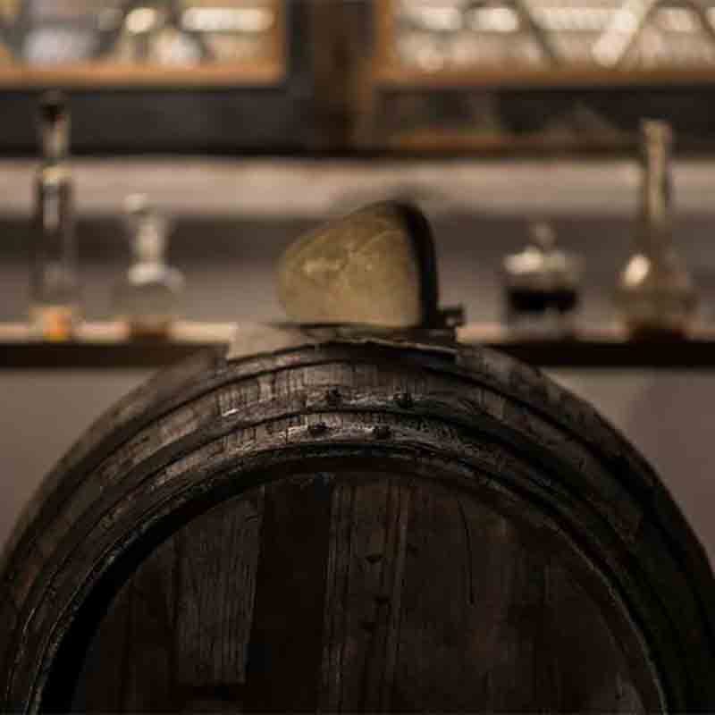 Holzfass in rustikalem Raum mit Flaschen im Hintergrund.