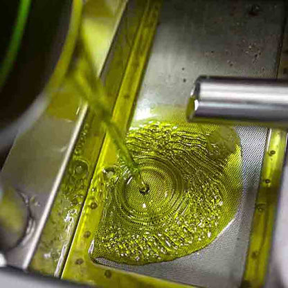 Olivenöl fließt durch Sieb in Produktionsanlage, Marke Intini.