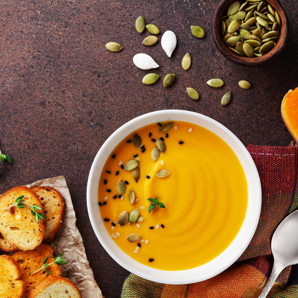 Kürbissuppe mit Kürbiskernen und geröstetem Brot auf Tisch.