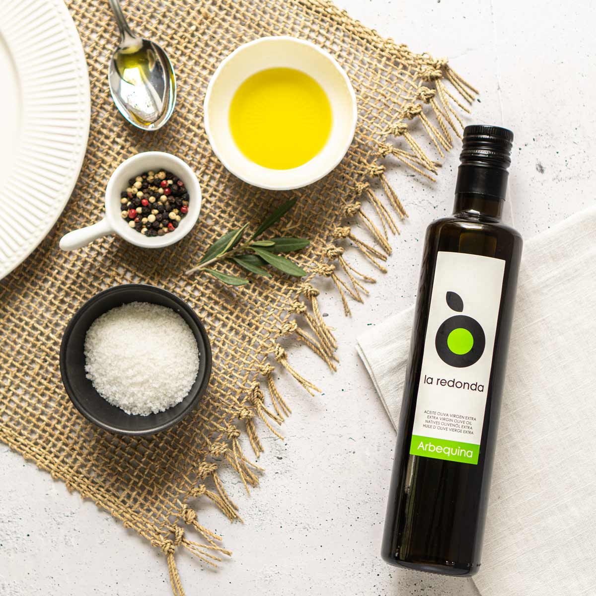 La Redonda Olivenölflasche mit Gewürzen und Geschirr arrangiert.