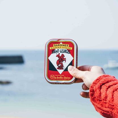 Hand hält Sardinen-Dose von La Belle-Iloise am Meer.