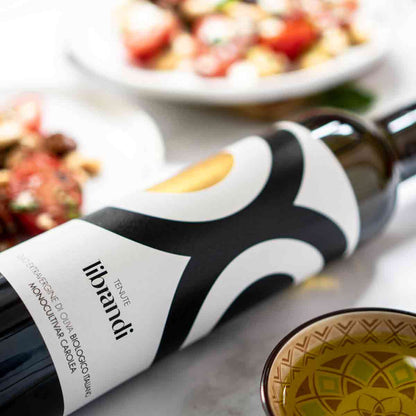 Librandi Olivenölflasche mit Speisen im Hintergrund.