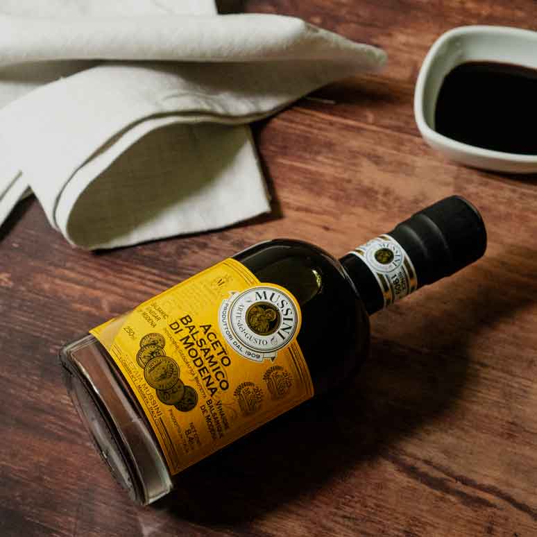 Mussini Aceto Balsamico Flasche auf Holztisch mit Tuch.