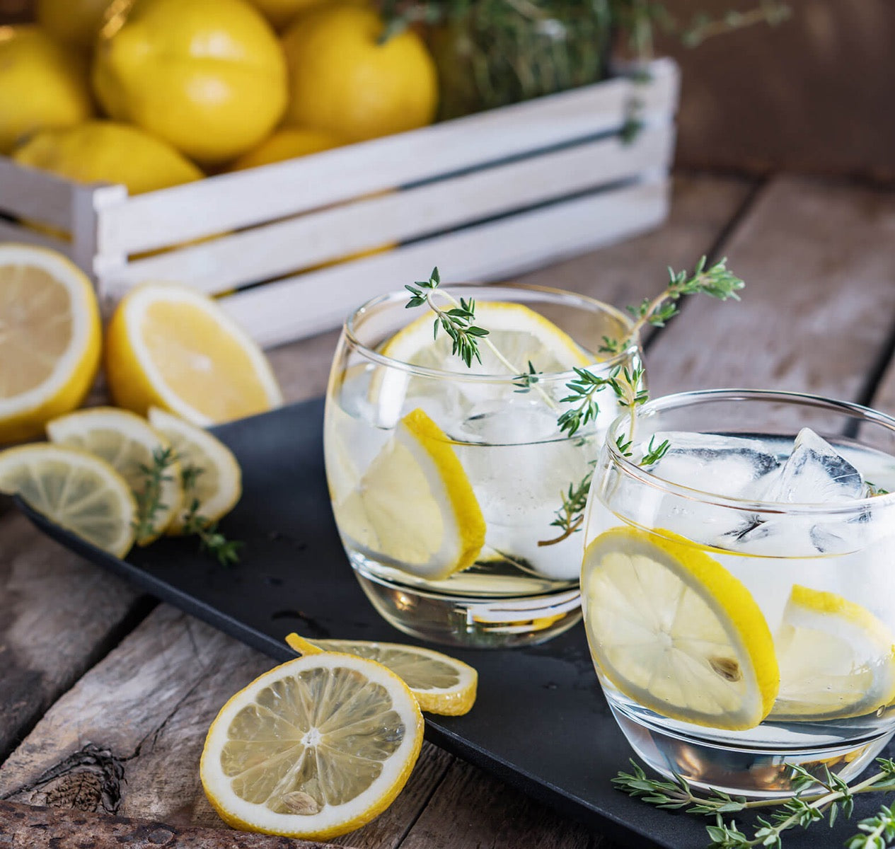 Zwei Gläser mit Zitronenscheiben und Thymian auf Tablett.