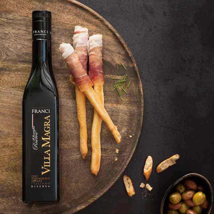 Olivenölflasche, Grissini, Oliven, Schinken auf Holzplatte, Marke Franci.