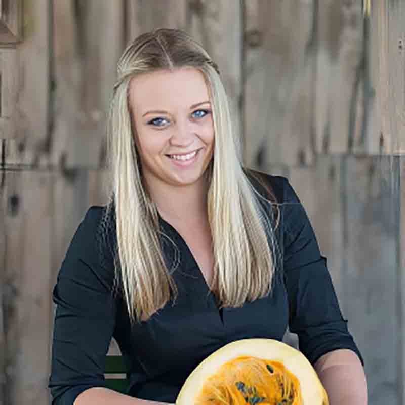 Freundlich lächelnde Frau aus dem Hartlieb Team mit aufgeschnittenem Kürbis in den Händen.