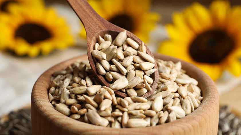Holzlöffel mit Sonnenblumenkernen in Holzschale, Sonnenblumen im Hintergrund.