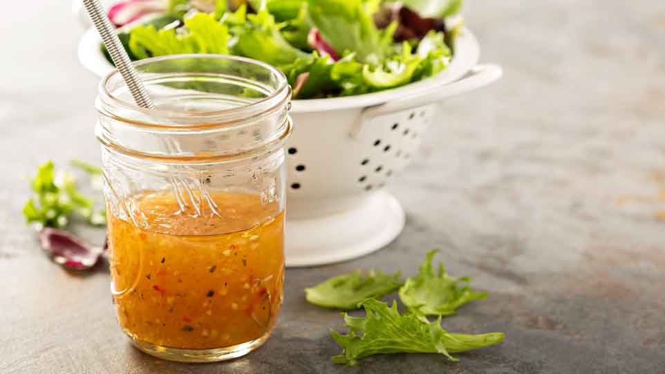 Salat mit Dressing im Glas, frische Blätter daneben.